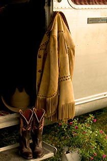 Fringed leather jacket and cowgirl boots set on doorstep of silver airstream